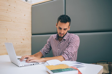 Focused man using laptop reading literature at workplace