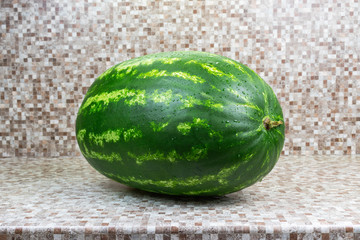 A whole green watermelon with bright stripes on the kitchen table.