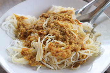 rice noodles dressing with fish coconut milk curry sauce and fresh vegetable on plate.