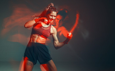 Cool female fighter in boxing bandages trains in studio in red neon light. Mixed martial arts...