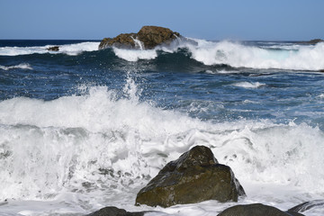 Seascape in the foreground large black rocks, in the background the horizon line and large waves