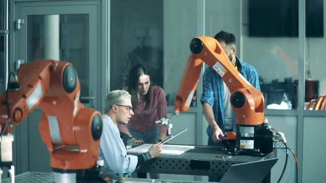 Cheerful people work with robotic arm on a table. Modern science laboratory.