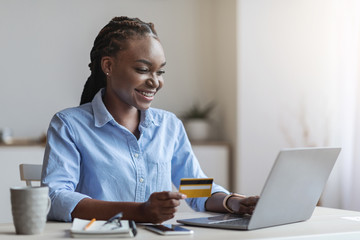 Young black businesswoman shopping online with laptop in office, using credit card
