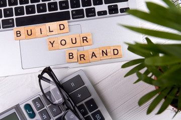 Flat lay build your brand slogan on a tablet pc touchpad. Calculator with glasses and plant. Isolated on white background.