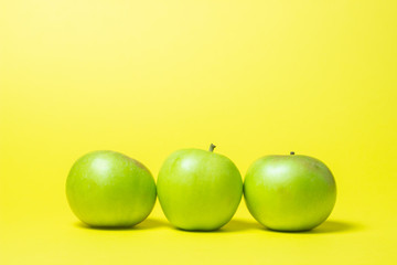 Three green apples on a yellow background. The apples are in a row.