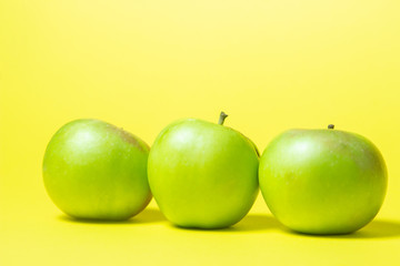 Three green apples on a yellow background. The apples are in a row.