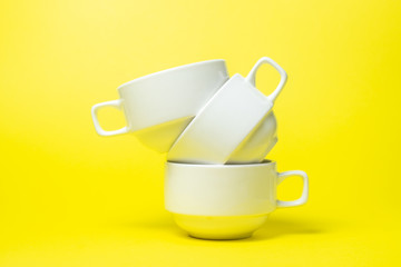 White cups on a yellow background. Three white cups are on top of each other. A tea set.