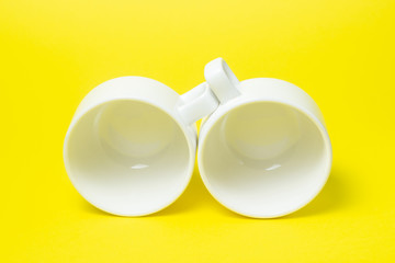White cups on a yellow background. Two white cups lie next to each other