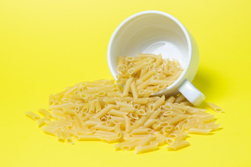 Pasta on a yellow background. The pasta spilled out of the cup. Italian Cuisine