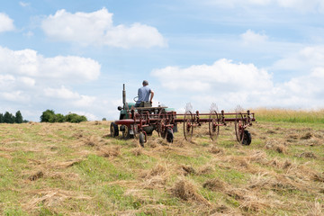 Man operating hay tedder machine to aerate the hay in the field