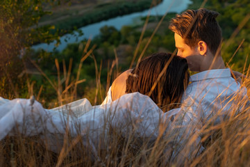 half portrait of a beautiful couple of guy and girl lying in the grass. Against the backdrop of the setting sun on a summer evening. White dress of the bride.