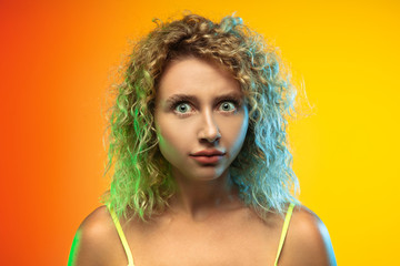 Shocked. Close up caucasian young woman's portrait on gradient studio background in neon. Beautiful female curly model in casual style. Concept of human emotions, facial expression, youth, sales, ad.