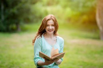 Beautiful Redhead Teen Girl Reading Book Outside In Summer Park