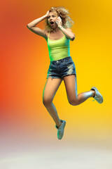 Shocked. Jumping caucasian young woman's portrait on gradient studio background in neon. Beautiful female curly model in casual style. Concept of human emotions, facial expression, youth, sales, ad.