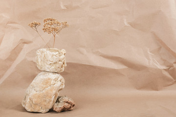 Layout made of from a pile of balancing stones and dry flower on craft beige background. Front view Copy space Monochrom