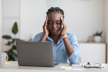 Overworked black businesswoman suffering from headache in office, massaging temples