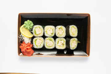 A portion of maki sushi with an assortment of Japanese side dishes in a rectangular ceramic plate on a white plate. Top view.