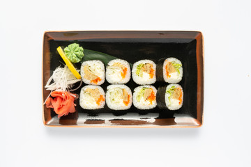 A portion of maki sushi with an assortment of Japanese side dishes in a rectangular ceramic plate on a white plate. Top view.
