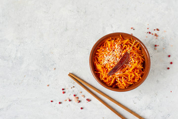 Asian or Korean pickled carrots, spicy salad of grated carrots with pepper, sesame and garlic in a clay salad bowl on a light background. Eastern vegetarian dish