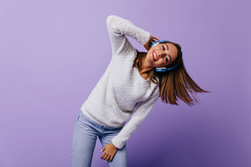graceful, energetic girl with short, smooth hair moves her torso while listening to her favorite song. Full-length portrait of European model on lilac background