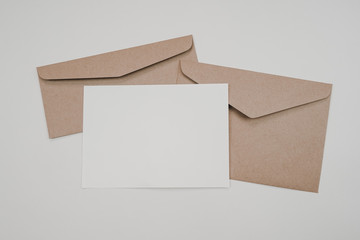 Blank white paper on the two brown paper envelope. Mock-up of horizontal blank greeting card. Top view of Craft paper envelope on white background. Flat lay of stationery. Minimalism style.