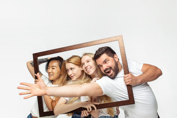 Photo frame. Group of adorable multiethnic friends having fun on white studio background. Copyspace. Diversity, inclusion, friendship and love concept. Different nationalities united with emotions.