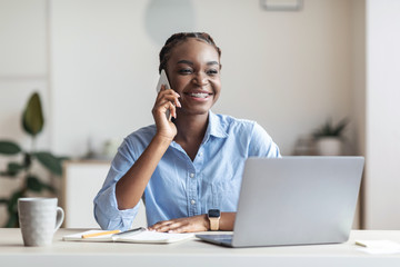 Black female entrepreneur talking on cellphone at workplace in office, consulting client