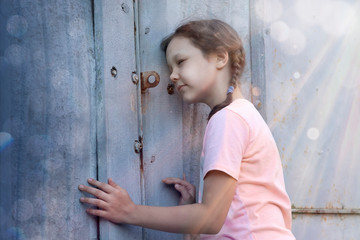 Little prying girl sparkles from the hole in the fence in the world outside its backyard.