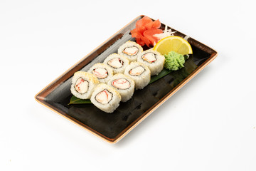 A portion of maki sushi with an assortment of Japanese side dishes in a rectangular ceramic plate on a white plate.