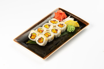A portion of maki sushi with an assortment of Japanese side dishes in a rectangular ceramic plate on a white plate.