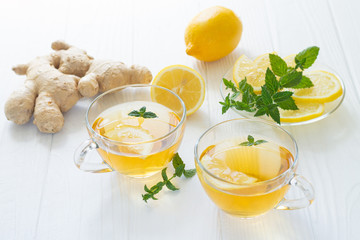 Two cups of hot tea with ginger, lemon and mint on a white wooden table
