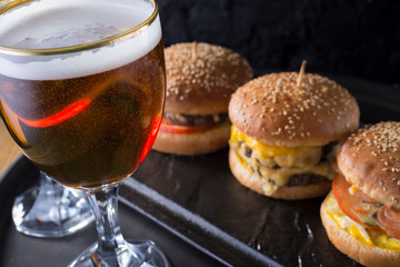 close-up, beer glasses with craft dark and light beer with foam, against a background of burgers, with a variety of ingredients, including shyomga, beef meat patty, cheese burger. In a rustic style