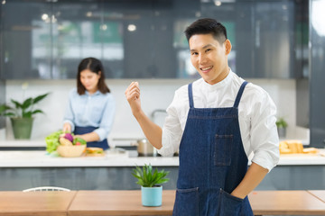 portrait asian man chef hand up in kitchen with woman cooking background. chef cooking concept.