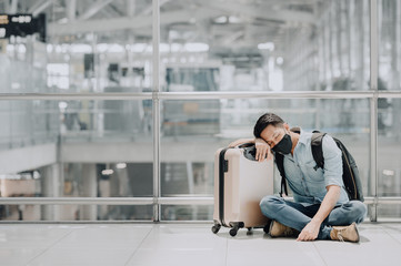 tried Asian man wearing face mask resting or sleeping on the floor of airport terminal waiting for...