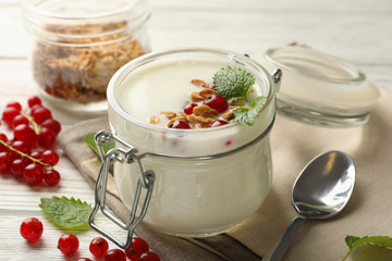 Yogurt with cranberry, granola and mint on white wooden background