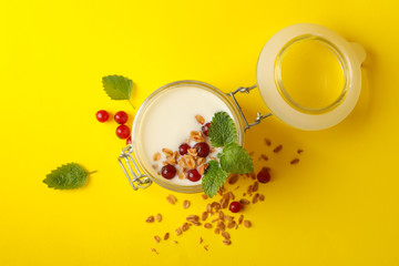 Glass jar of sour cream yogurt with cranberry, mint and granola on yellow background