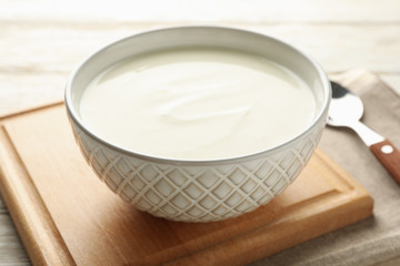 Sour cream yogurt, spoons and napkin on white wooden background