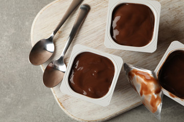 Board with plastic cups of yogurt and spoons on gray background
