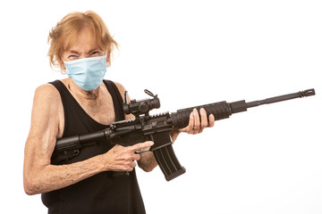 Senior woman holding a weapon, looking at the camera while wearing a mask and squinting.