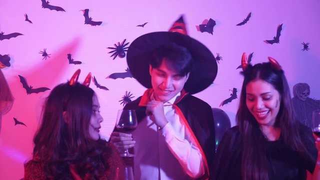Normal view, hand held, Medium shot of 3 Asian teens in Halloween costume dancing, holding wine glass at disco party