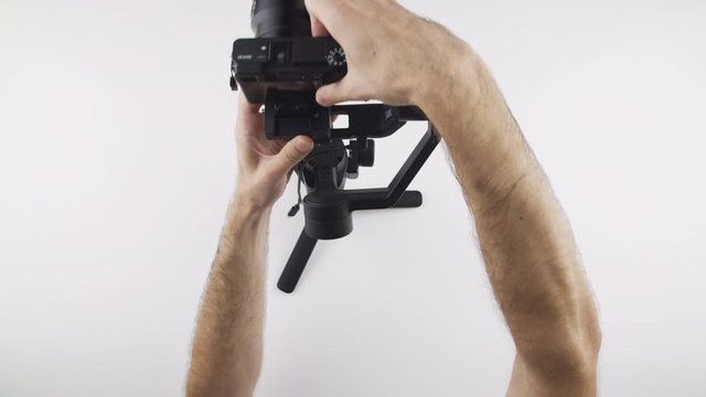 Top view, caucasian man assemble electronic gimbal RONIN SC and stabilize Sony mirrorless camera with his hand on white desk.