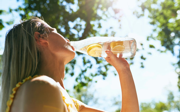 Bottom closeup view of a pretty blonde young woman enjoying drinking lemonade while resting in the park on sunlight. Female on a picnic having a detox drink.