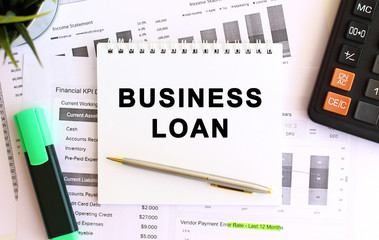 Notepad with text BUSINESS LOAN on a white background, near calculator and office supplies. Business concept.