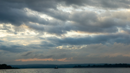 dark grey clouds over a dark grey lake with silhouette of a light house 