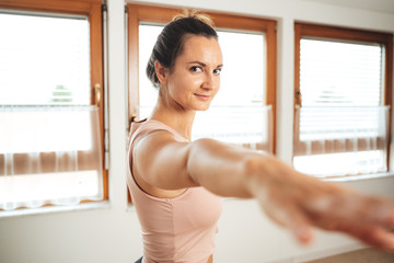 Portrait of sporty young woman in warrior pose practicing yoga at home
