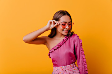 fragile, shy woman of 21 years old in blouse with bare shoulder smiles in friendly way, looking down. closeup portrait of stylish model on isolated background