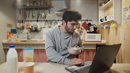Business man working laptop computer and eats Corn Flakes Cereal at home kitchen.