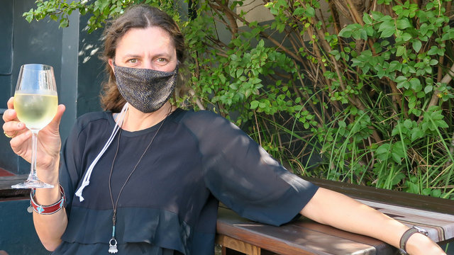 Female Tourist with fce mask drinking wine in restuarant.