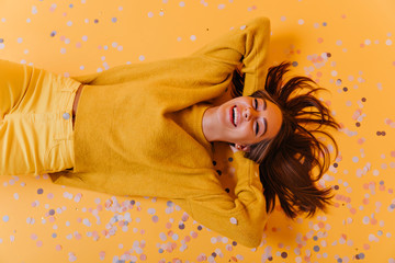 Magnificent girl in yellow pants lying on purple confetti. Overhead portrait of enthusiastic...