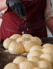 a Baker in a red apron sprinkles dough pieces that are lying on a baking sheet